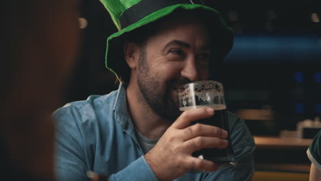 portrait of happy man in irish hat drinking a beer mug and talking with friends in a pub