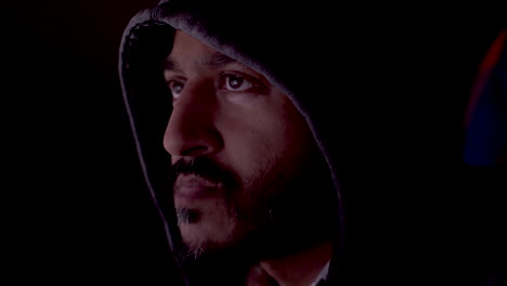 a face of a middle-aged brown-eyed man wearing a hoodie. man is browsing the internet in front of the screen. the screen light reflects on the man's face