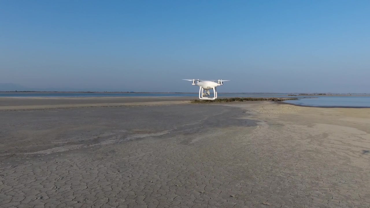 Drone bianco che sorvola terra secca e screpolata vicino all'acqua