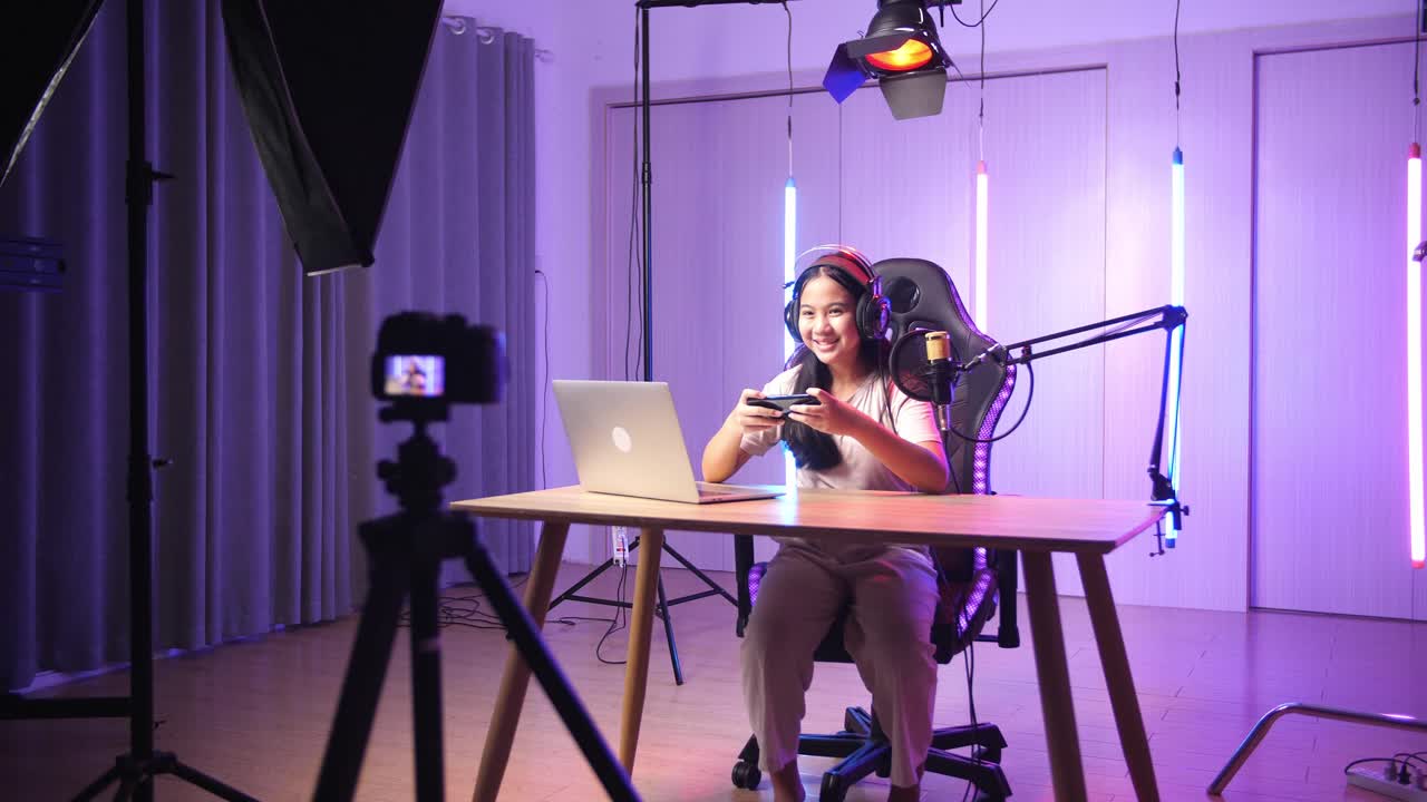 Excited Asian Kid Girl Playing Video Game With Mobile Phone Then Smiles To Camera While Live Stream, Professional Light Equipment