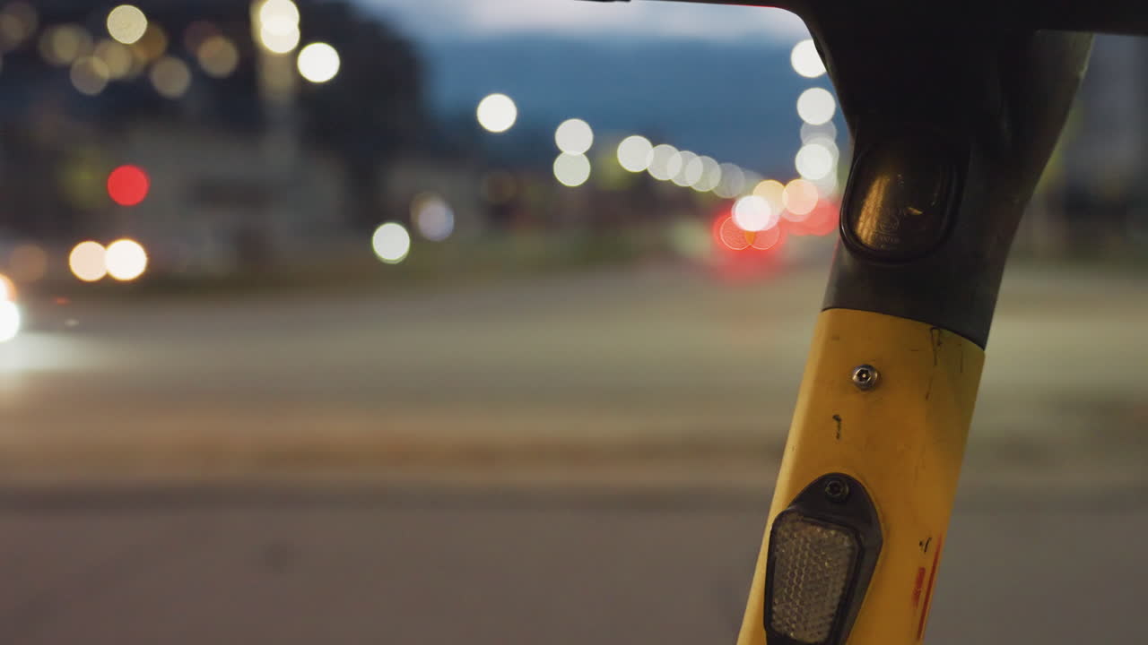 Close up view of yellow bike stem at night with blurred city background, glowing street lights and fast-moving car lights in soft focus creating dynamic urban atmosphere with contrast and motion