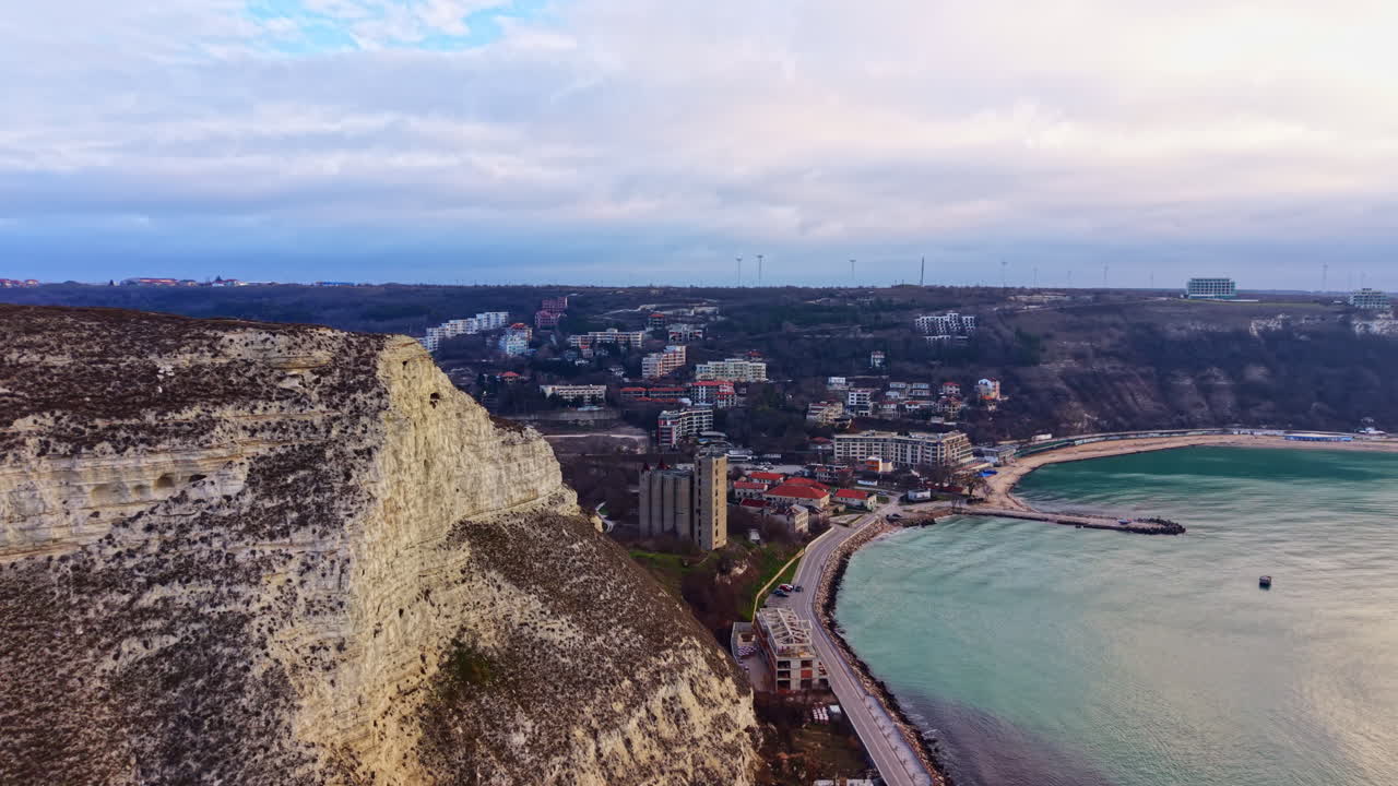 Scogliere a picco su una cittadina balneare con un porto e turbine eoliche durante il giorno con nuvole nel cielo