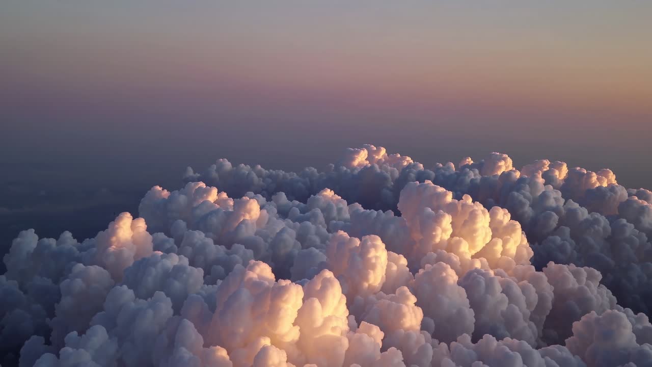 Aerial video captures fluffy clouds at sunset, with warm light highlighting their texture