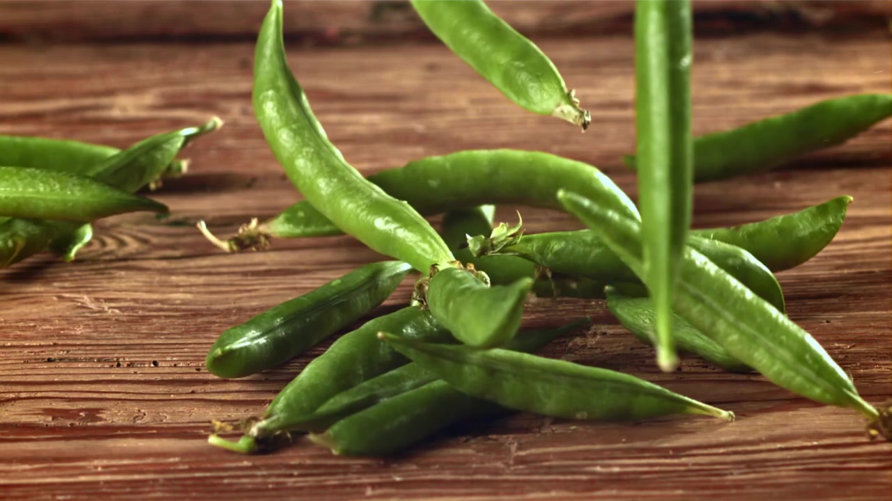 Fresh Green Pea Pods Falling onto a Rustic Wooden Table in Slow Motion