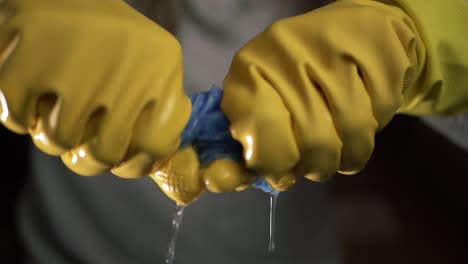 hands wringing out cleaning cloth wearing yellow rubber gloves medium shot