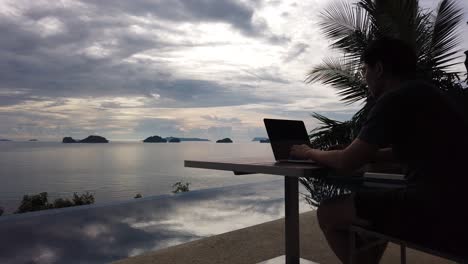 Asian-man-working-on-the-laptop-by-the-pool---side-view