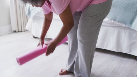 Portrait-of-senior-african-american-woman-holding-yoga-mat-smiling-at-home