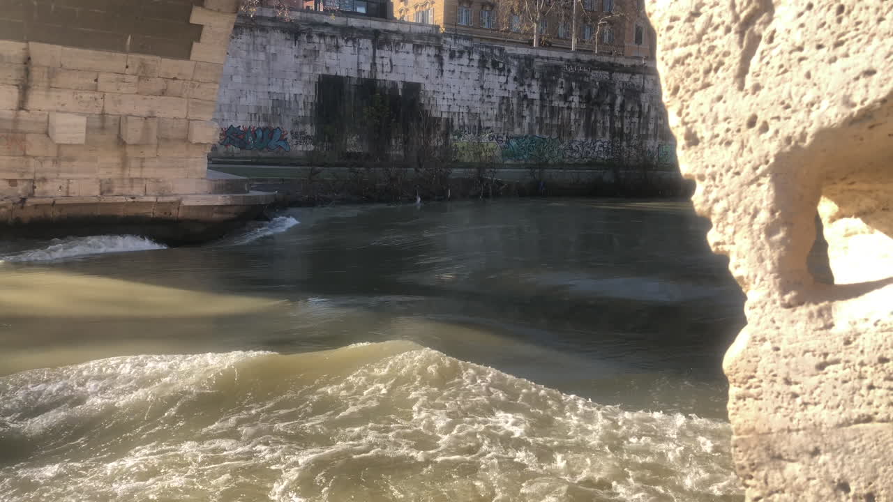 Iconic Italian river Tiber flowing under an old stone bridge in Isola Tiberina