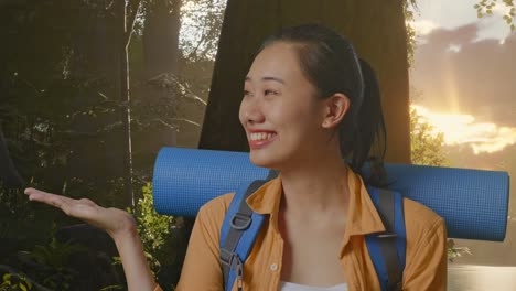 primer plano de una excursionista asiática con una mochila de montañismo sonriendo y señalando hacia un lado mientras explora la naturaleza forestal
