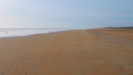 Amplia-Playa-De-Arena-En-Saint-Jean-de-Monts,-Francia,-Con-Figuras-Distantes-Y-Suaves-Olas.