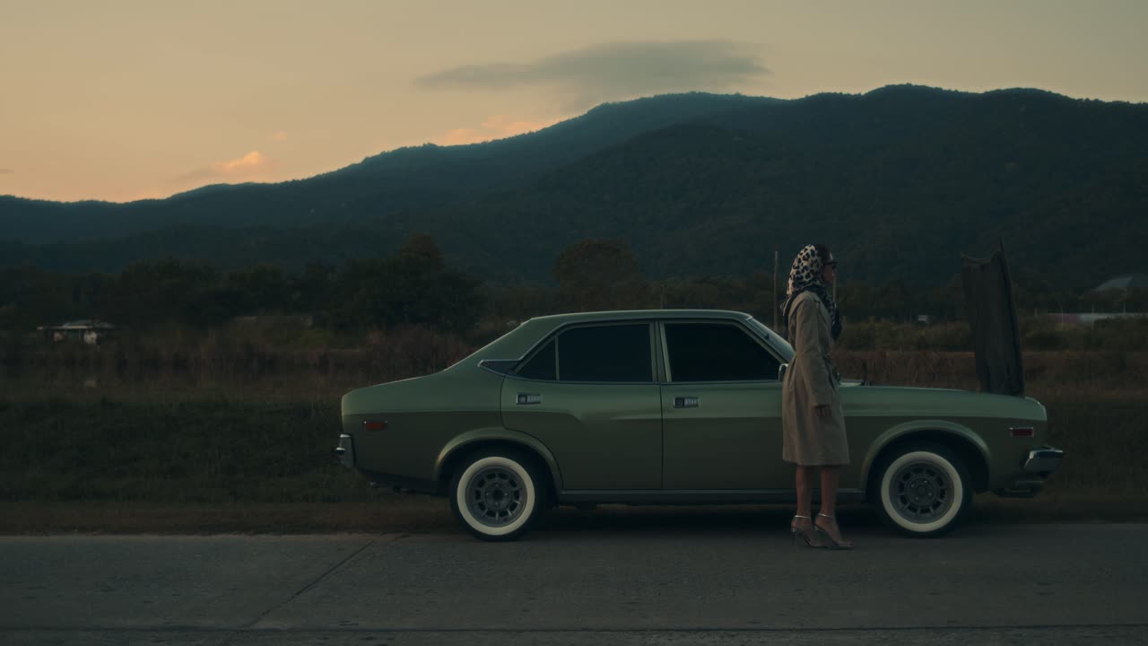 Woman by a vintage car in the mountains at sunset