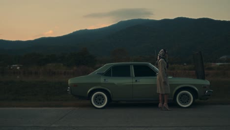 woman by a vintage car in the mountains at sunset