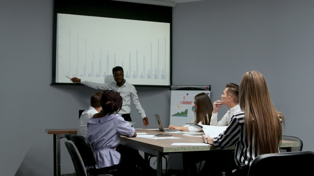 el entrenador afroamericano da una presentación corporativa para los empresarios en la oficina, el empresario de piel oscura presenta un nuevo plan de negocios en la pizarra, hablando con los clientes escuchando al orador en la reunión