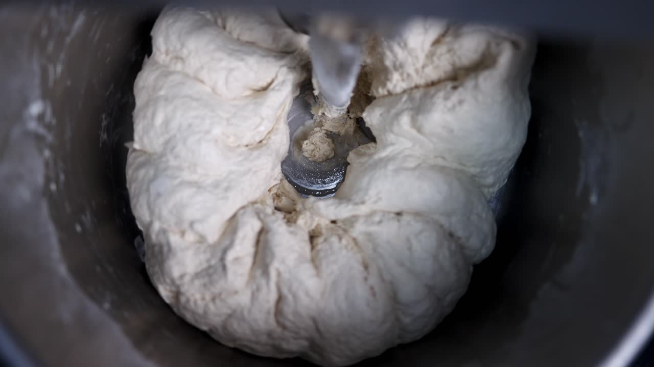 Top view in slow motion of dry pizza dough in a mixing machine bowl under clear and nice atmosphere.