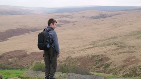 young boy outdoors standing on a countryside hill top, admiring the moorland views