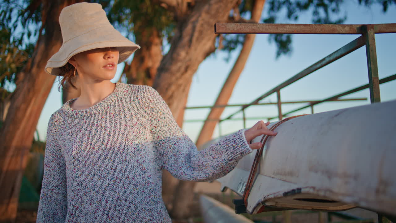 una mujer bonita camina en botes a la orilla del río en un primer plano de campamento. una chica de viaje posando con un sombrero