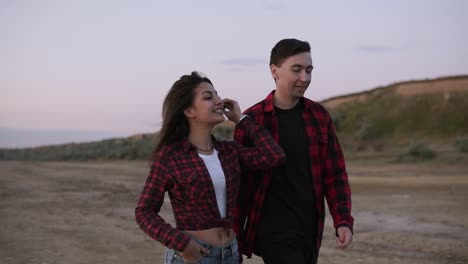 Beautiful-young-couple-in-plaid-shirts-are-walking-outdoors-on-a-sandy-teritory-in-the-evening.-Caucasian-brunette-couple,-friendship,-hanging-out-together