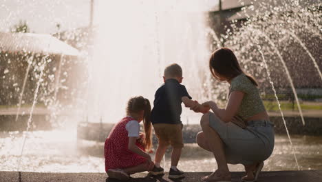 Mother-and-little-boy-with-girl-sit-on-parapet-near-fountain