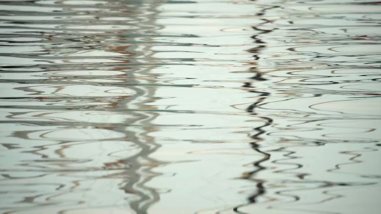 Superficie del agua creando una textura abstracta con suaves ondas, reflejando líneas verticales de luz y sombra, sugiriendo tranquilidad.