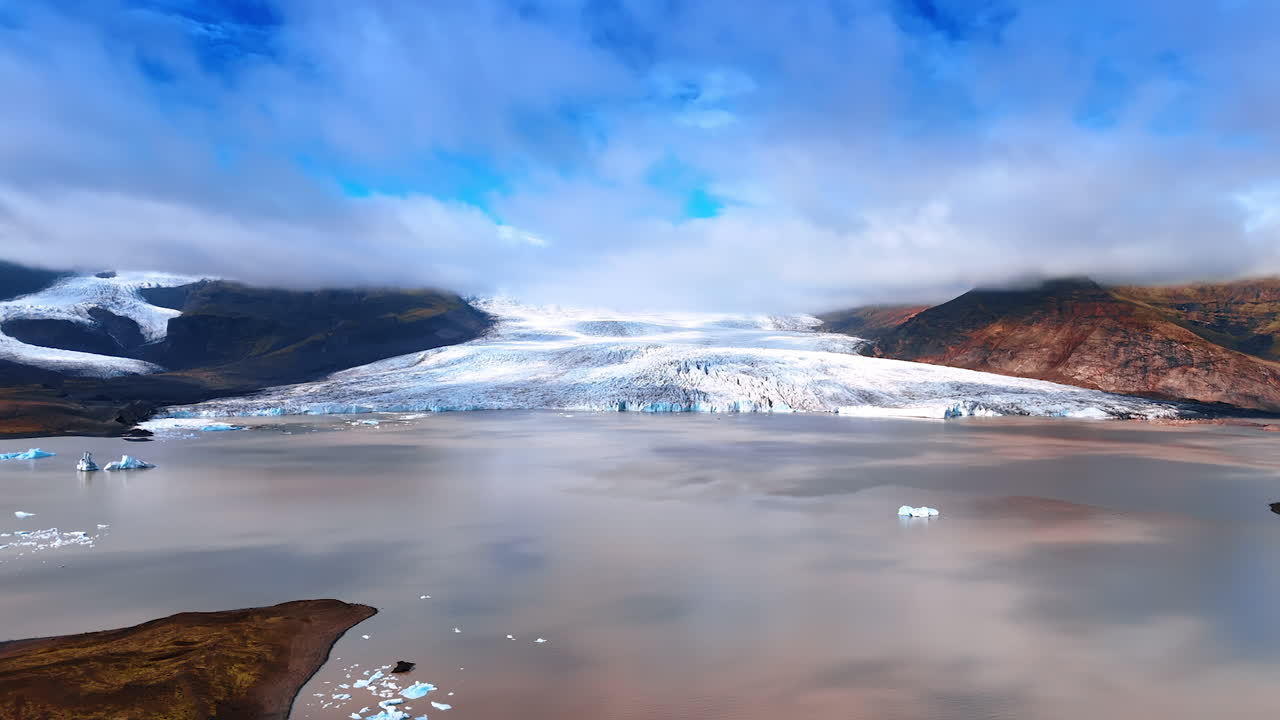 Rocky landscapes, waterscape and amazing glacier descending into water. Dense cloudscape hanging above the mountains. Iceland from drone.