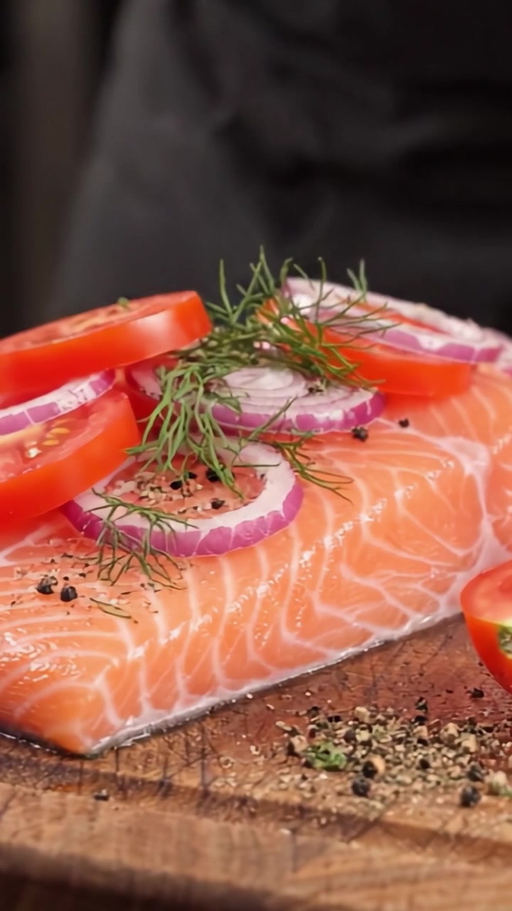 Filetto di salmone appena affettato guarnito con pomodoro, cipolla e aneto, perfettamente preparato per un delizioso pasto imminente.