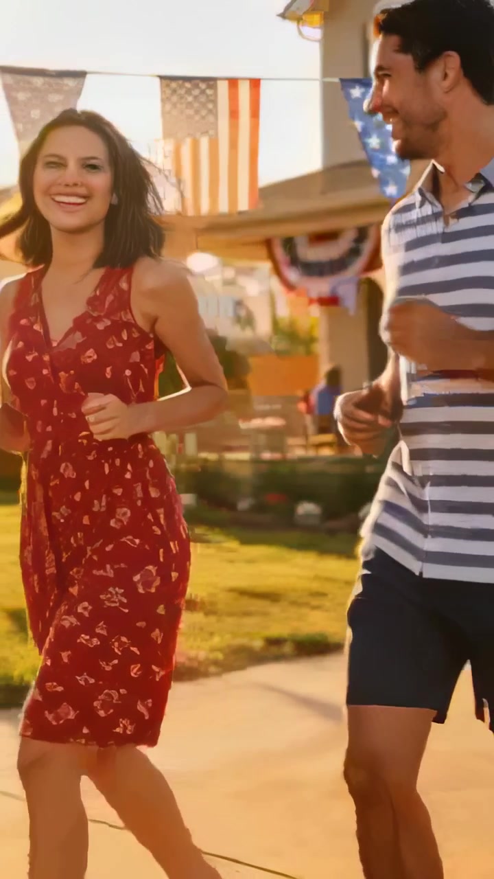 Video verticale: Famiglia che corre e inizia una parata in giardino per una festività, con una donna in abito rosso che sventola bandiere.