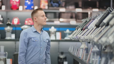 a young man in a shirt chooses a blender for his kitchen in a consumer electronics store