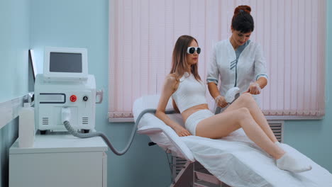 young woman in white bathrobe on laser hair removal procedure in beautician clinic slow motion. doctor removes hair from legs or body of patient. concept