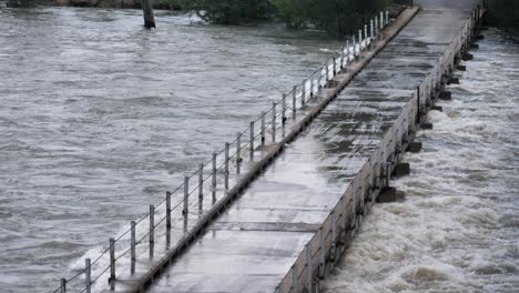 氾濫する川を渡る低い一車線の橋には、甲板まで水が流れています