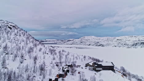 Dron-Cinemático-Aéreo-En-Movimiento-Hacia-Atrás-Disparado-A-Través-De-Un-Valle-De-Invierno-Cubierto-De-Nieve-Blanca-Con-Casas-De-Pueblo-Rodeadas-Por-Una-Impresionante-Cordillera-En-Un-Día-Nublado