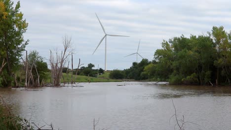 un estanque de granjeros inundado rodeado de árboles con turbinas eólicas en la distancia en un día nublado en nebraska, ee.uu.