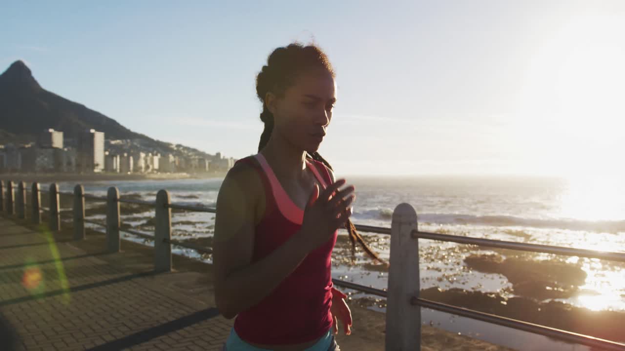 African american woman running on promenade by the sea at sundown