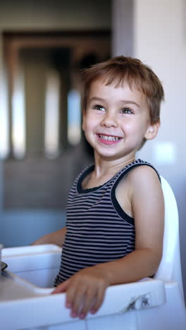 cute smiling caucasian kid sits at high chair. mom's hand passes a full spoon to a baby but he refuses to eat. vertical video.