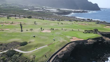 Retirada-Aérea-De-Un-Impresionante-Campo-De-Golf-Con-Vistas-Panorámicas-Del-Océano-Azul-Al-Mediodía