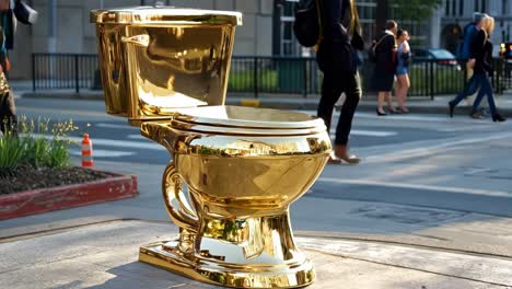 a woman walking past a gold toilet on a city street