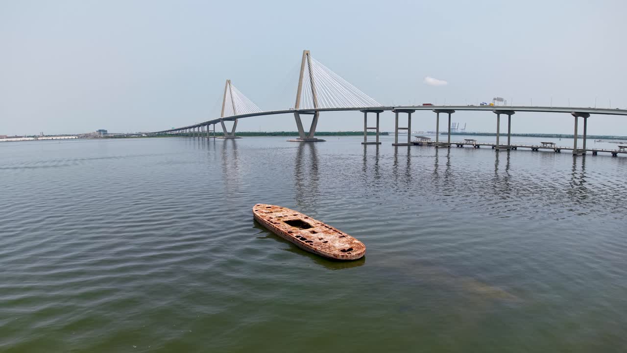 Un filmato realizzato con un drone mostra una veduta aerea di una piccola imbarcazione su acque calme sotto un grande ponte strallato a Charleston, nella Carolina del Sud, con il porto e lo skyline sullo sfondo.
