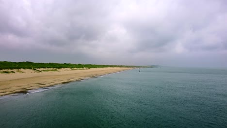 Aerial-shot-flying-over-the-ocean-looking-back-at-a-golden-sand-beach-in-the-UK