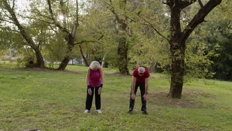 Active-senior-couple-doing-morning-stretching-physical-exercises-in-park.-Fitness-family-leisure