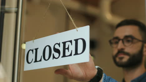 close-up view of young man turning over a open" signboard in coffee shop door"