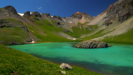 drone cinematográfico de hielo cuenca del lago silverton isla lago verano agua azul agua clara tundra alpina impresionante cordillera de las montañas nieve flores silvestres de día hermoso movimiento lento hacia la izquierda