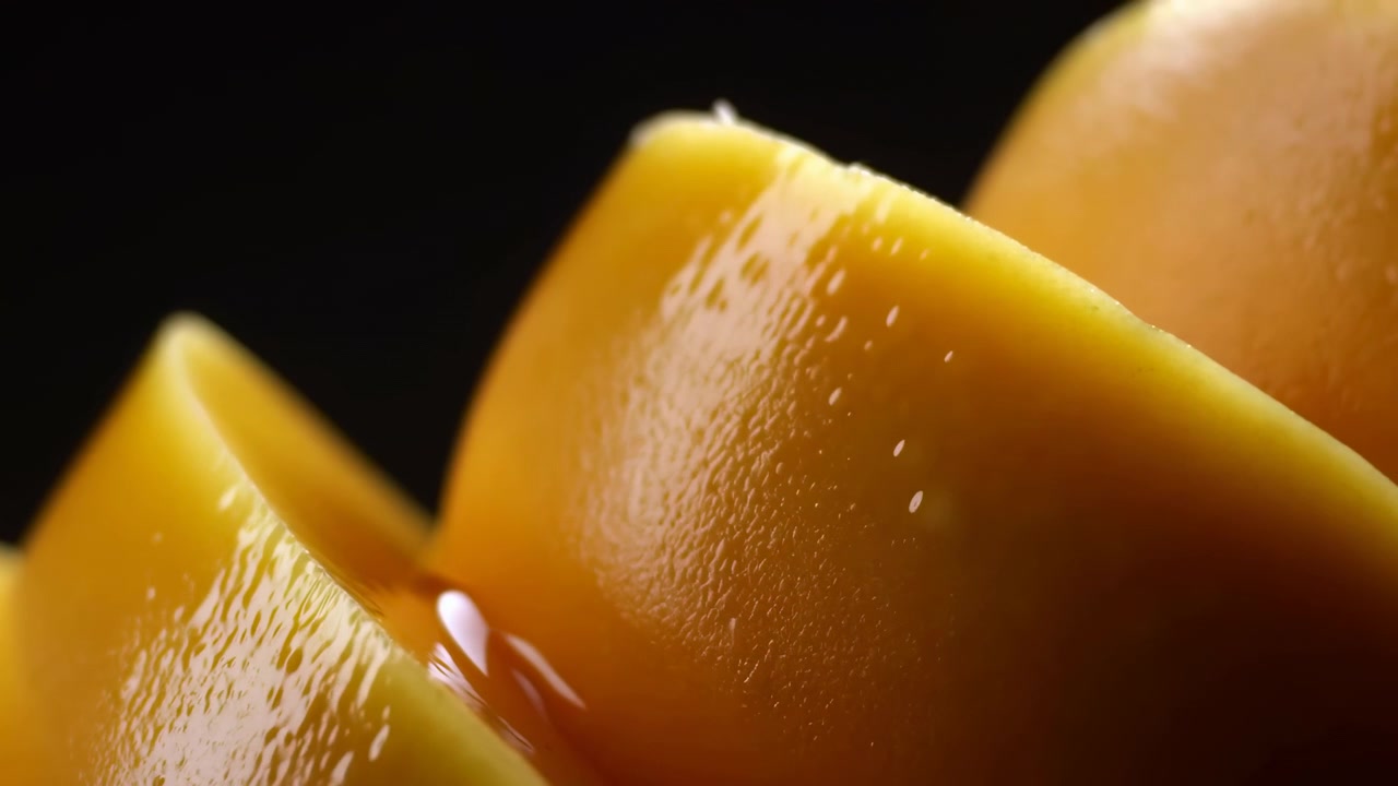 Vista macro dal basso di fette di mango lucide con superfici riflettenti bagnate, piccoli pori della buccia e una piccola goccia di liquido che si raccoglie nella piega tra gli strati, creando un dettaglio di cibo tropicale fresco.