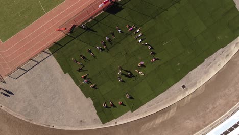 Niños-Haciendo-Sentadillas-En-La-Pista-De-Atletismo,-Antena-Giratoria-De-Arriba-Hacia-Abajo