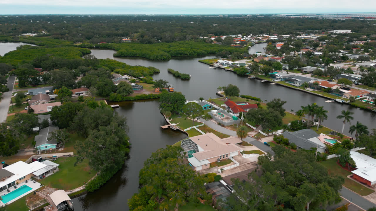 Neighborhood built along and around canals with trees lining waterway and bright roofs, aerial dolly along water