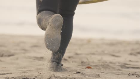 SLOW-MOTION,-a-surfer-in-full-wetsuit-runs-on-the-golden-sand-of-Unstad-beach-with-his-surf-board-towards-the-sea,-Lofoten-Islands,-Norway