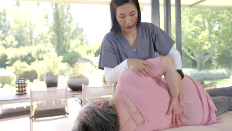 assisting with stretching exercise, physiotherapist helping senior woman at home
