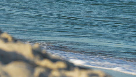 Close-up-of-ocean-waves-crashing-gently-on-rocky-shoreline-with-clear-blue-water