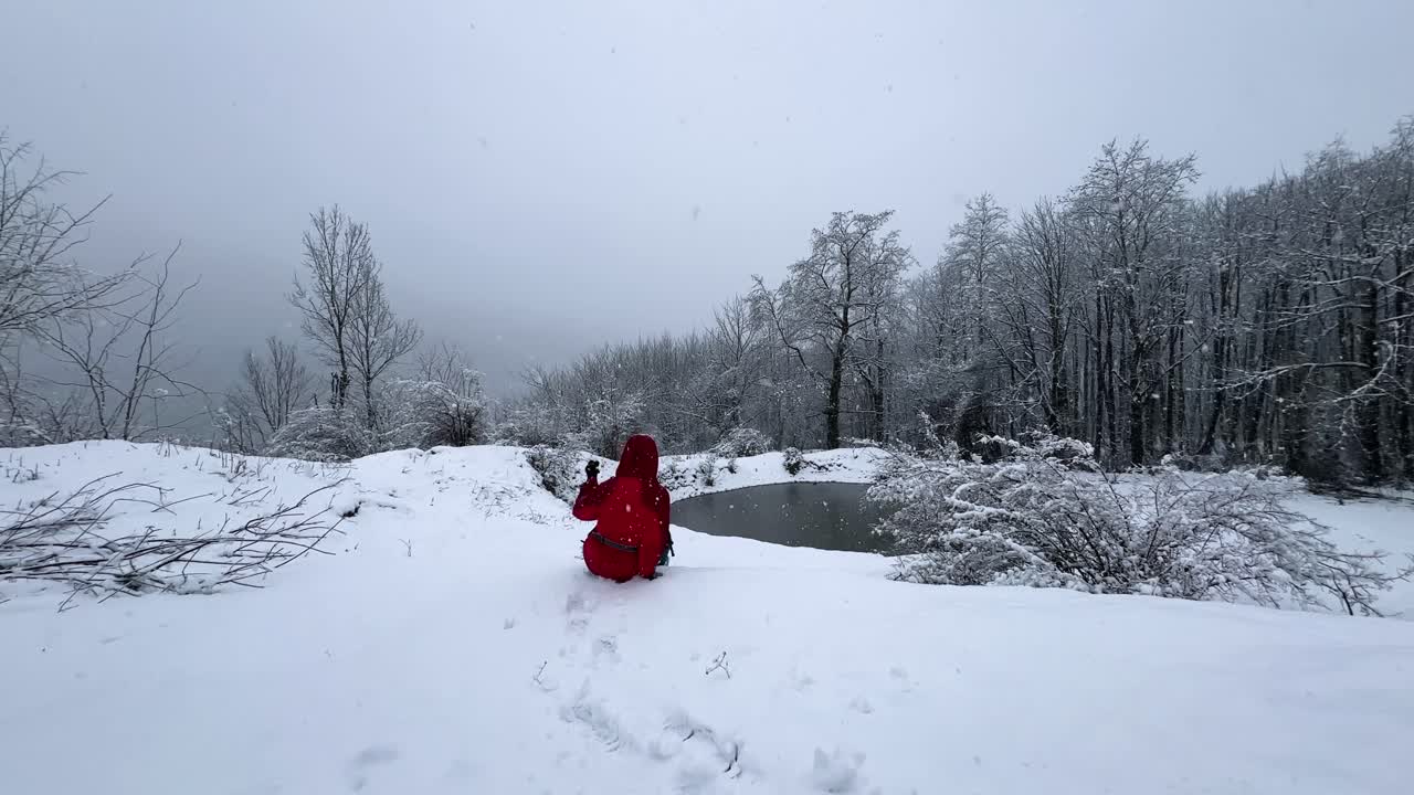 Woman with red jacket is sitting in a wonderful viewpoint in winter frozen lake mountain forest scenic landscape snowfall hiking adventure countryside nature Hyrcanian Iran adrenaline outdoor activity