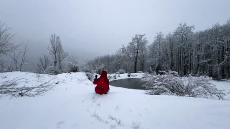 woman with red jacket is sitting in a wonderful viewpoint in winter frozen lake mountain forest scenic landscape snowfall hiking adventure countryside nature hyrcanian iran adrenaline outdoor activity