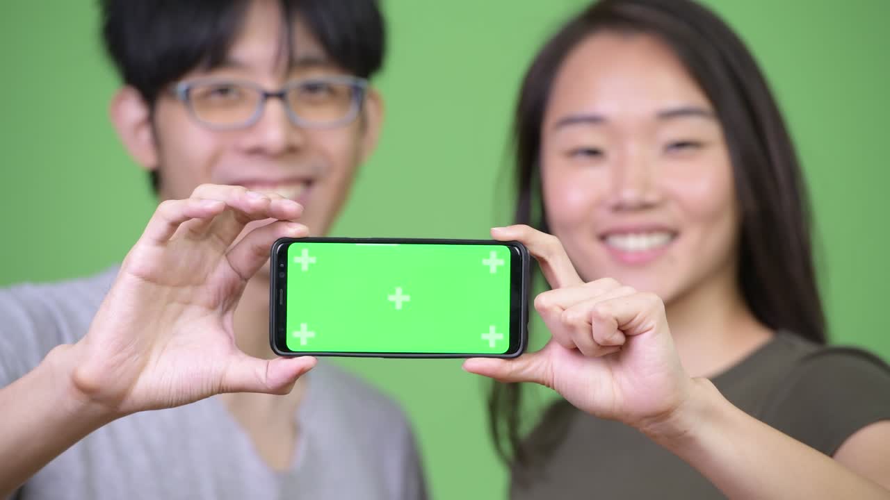 젊은 아시아 커플이 함께 전화를 보여주고 있습니다.