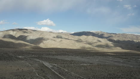 Montañas-Desérticas-Y-Sombras-De-Nubes-Con-Carretera-A-Distancia